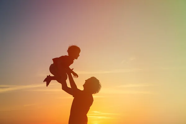 Vader en kleine zoon silhouetten spelen bij zonsondergang — Stockfoto