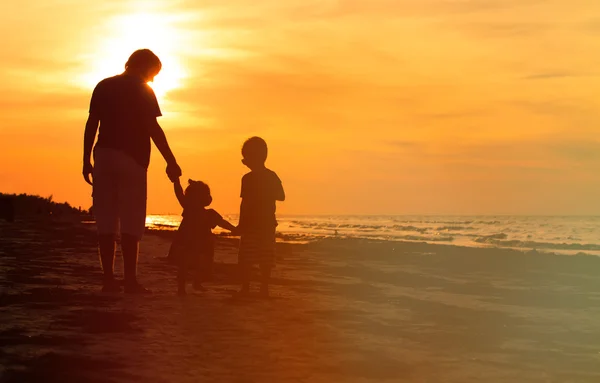 Padre e due bambini che camminano sulla spiaggia al tramonto — Foto Stock