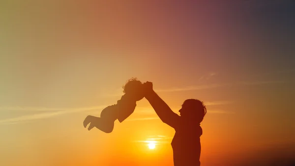 Vader en kleine dochter spelen silhouetten bij zonsondergang — Stockfoto