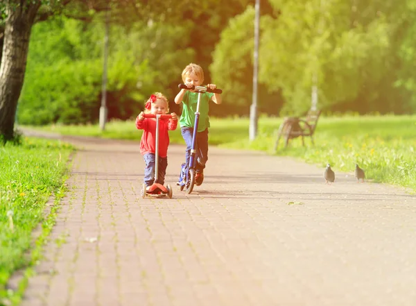 Мальчик и девочка катаются на скутерах в летнем парке — стоковое фото