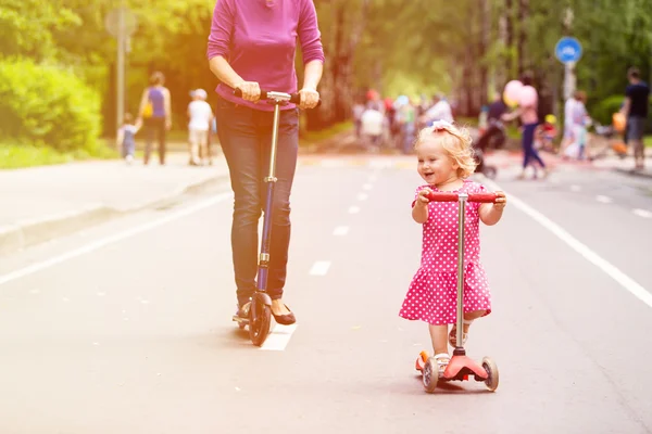Boldog kis lány és anya a szkuterek (robogók), a város — Stock Fotó