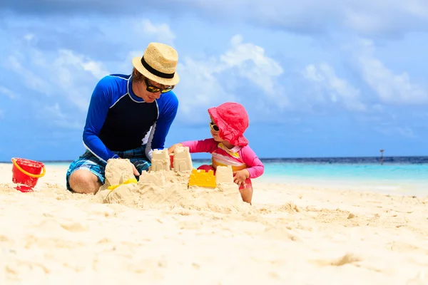 Отец и маленькая дочь играют с песком на пляже — стоковое фото