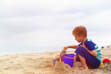 Küçük çocuk yaz kumsalında kumla oynuyor.