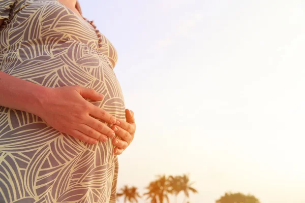 Mulher grávida no pôr do sol praia tocando sua barriga com amor — Fotografia de Stock