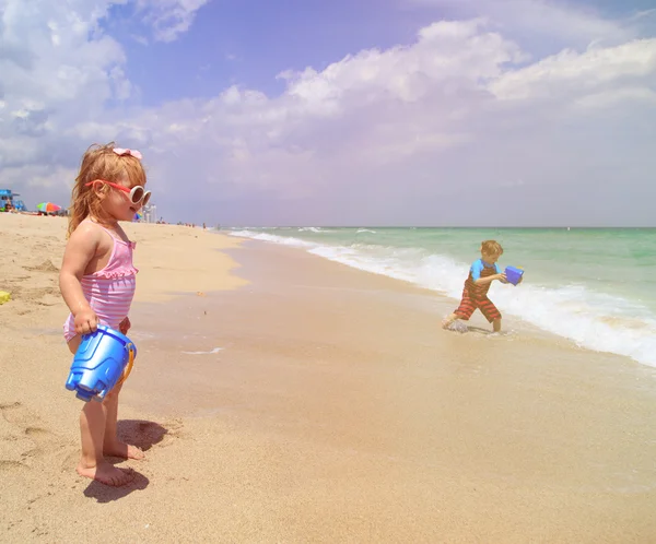 Schattig klein meisje en jongen spelen met water op het strand — Stockfoto