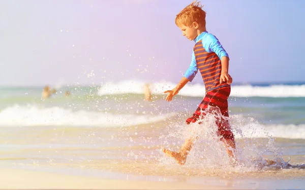 Маленький хлопчик біжить бризкаючи воду на пляжі — стокове фото