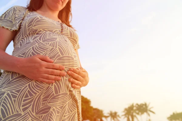 Mulher grávida no pôr do sol praia tocando sua barriga com amor — Fotografia de Stock