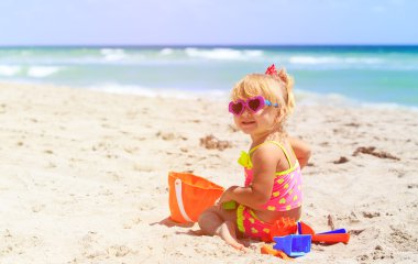 Tatlı küçük kız kumsalda kumla oynuyor.