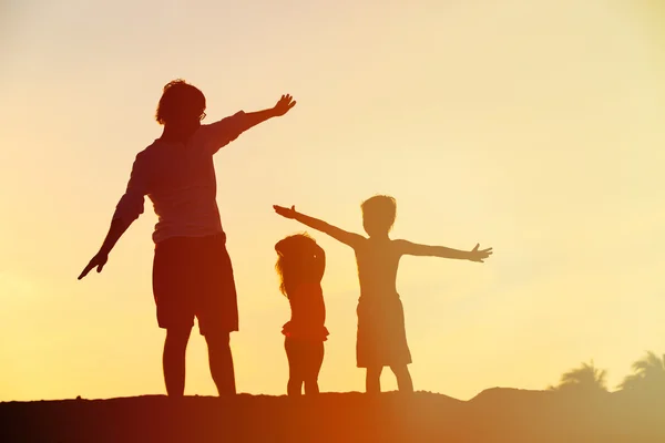 Father with son and daughter silhouettes play at sunset — Stock Photo, Image