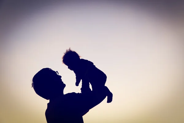 Silhouetten van vader en kleine baby spelen bij zonsondergang — Stockfoto