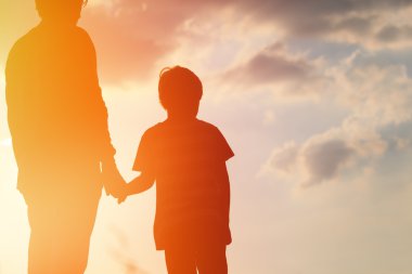 Gün batımında el ele tutuşan baba ve oğulun silueti.