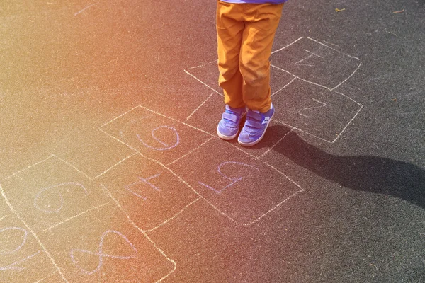 เด็กน้อยเล่นฮ็อปสก็อตช์บนสนามเด็กเล่น — ภาพถ่ายสต็อก