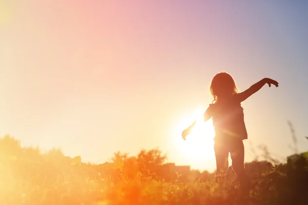 Silhuetten av glad liten flicka spela vid solnedgången — Stockfoto