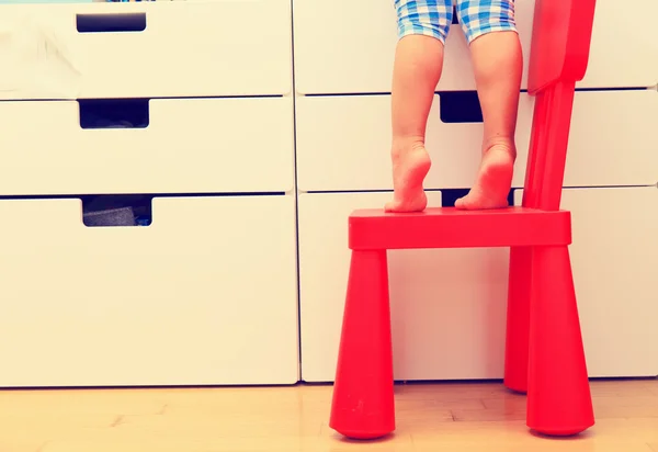 Kids safety concept- little girl climbing on baby chair — Stock Photo, Image