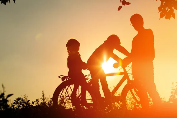 Батько з двома дітьми катається на велосипеді на заході сонця — стокове фото