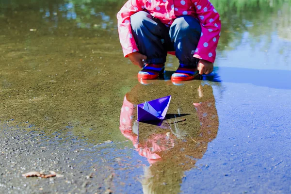 Dziewczynka bawi się papierowymi łódkami w kałuży — Zdjęcie stockowe