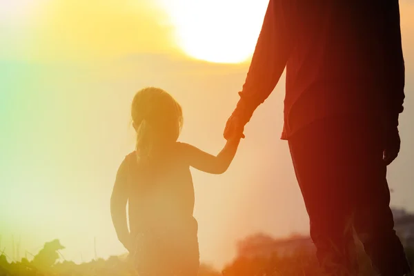 Silhueta de pai e filha de mãos dadas ao pôr do sol — Fotografia de Stock