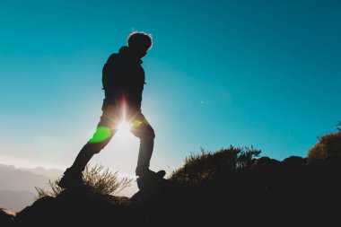 Gün batımı dağlarında yürüyüş yapan genç bir çocuğun siluetleri.