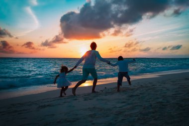 Mutlu baba ve iki çocuk gün batımında sahilde oynuyorlar.