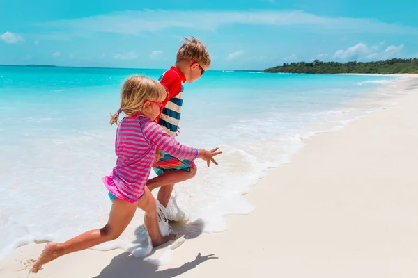 Gelukkig meisje en jongen run spelen met golven op het strand — Stockfoto