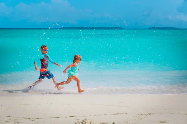 Gelukkig klein meisje en jongen rennen en spelen met water op het strand — Stockfoto