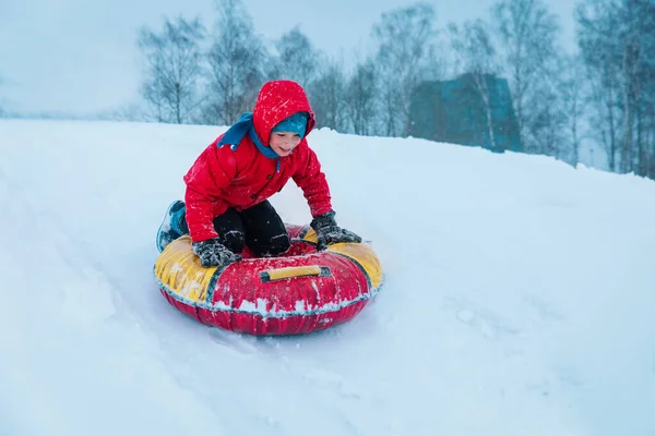 Glückliches Kind rutscht im Winter auf Schlauch den Schneehügel hinunter — Stockfoto