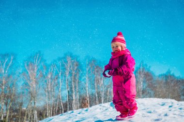 Şirin küçük kız doğada karla oynuyor.