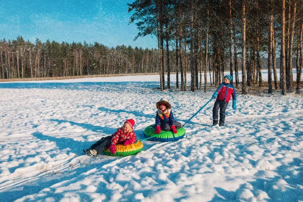 Χαρούμενα παιδιά γλιστράνε στο χιόνι του χειμώνα, αγόρια και κορίτσια διασκεδάζουν έξω — Φωτογραφία Αρχείου