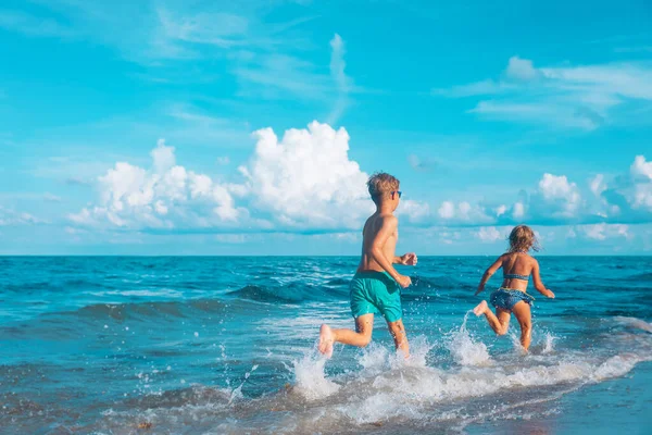 Happy girl and boy run, kids play with waves on beach — Stock fotografie