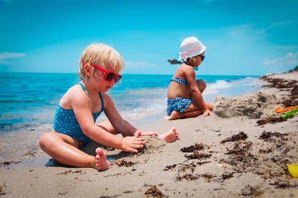 Cute little girls play with sand on beach — Stock Photo, Image