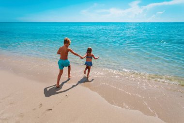 Mutlu çocuk ve kız yüzmek için plaja koşar, aile tatili