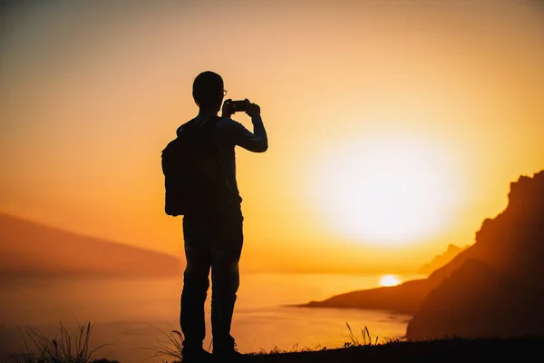 Silhouette eines Mannes mit Handy beim Fotografieren im Freien während des Sonnenuntergangs in den Bergen — Stockfoto