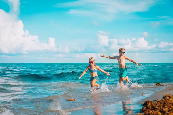 Маленькая девочка и мальчик бегают и играют с водой на пляже — стоковое фото