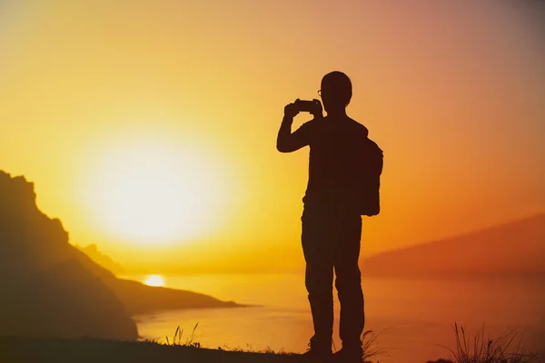 Silhouet van een man met een mobiele telefoon die buiten foto 's maakt bij zonsondergang in de bergen Stockfoto