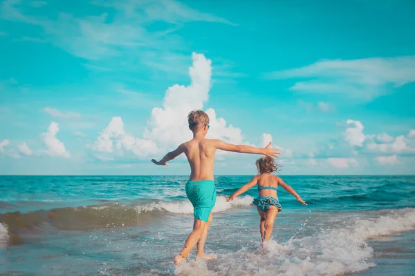 Klein meisje en jongen rennen en spelen met water op het strand Stockafbeelding