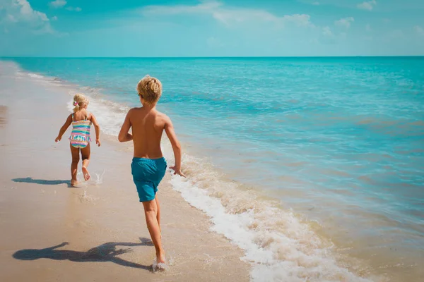 Gyerekek futni, fiú és lány szórakozni a trópusi strandon — Stock Fotó