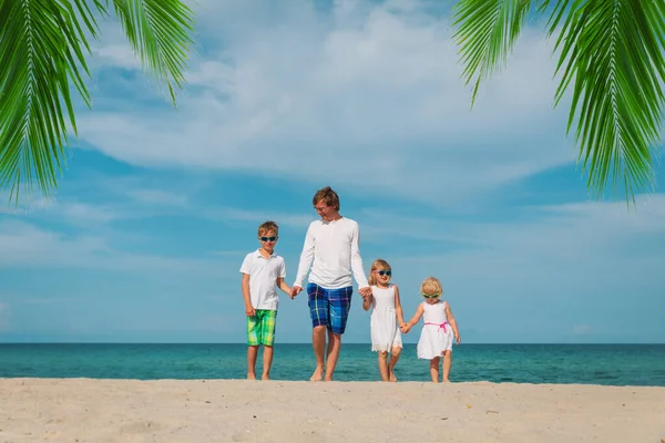 Pai feliz e três crianças andando na praia Imagens Royalty-Free