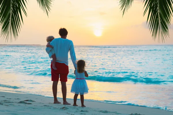 Vader en kinderen wandelen op het strand bij zonsondergang — Stockfoto