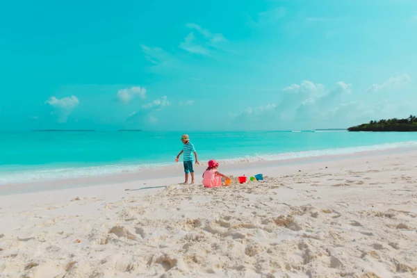 Счастливые мальчик и девочка играют с песком на пляже — стоковое фото