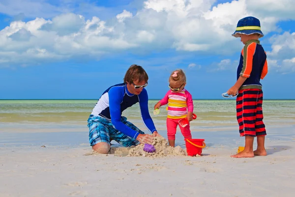 Father and two kids playing with sand on the beach — Stock Photo, Image