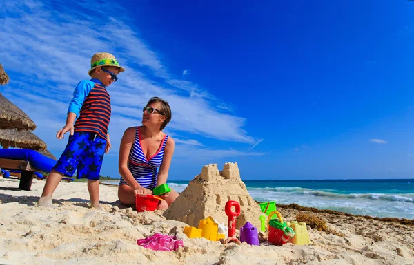 Matka a syn písku hrad na tropické pláži — Stock fotografie