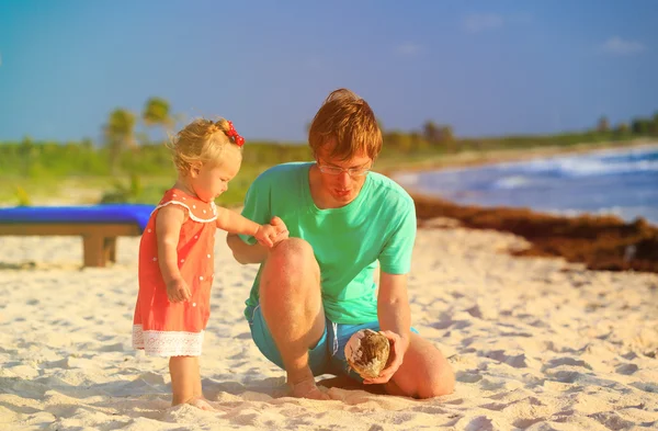 Vader en dochtertje kijken naar kokosnoot op het strand — Stockfoto
