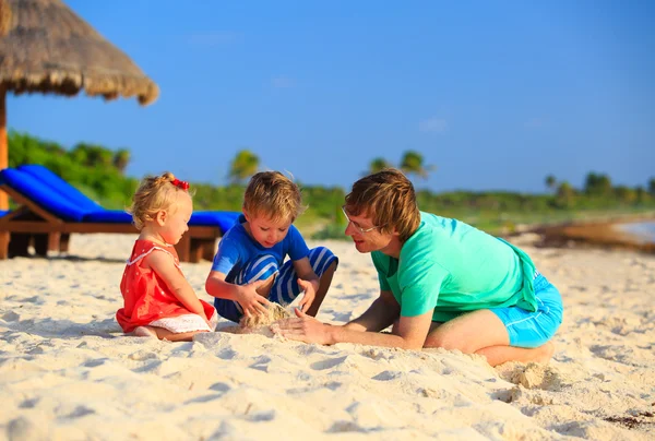 Father and two kids playing with sand on beach — Stock Photo, Image