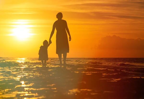 Mor och liten dotter går på stranden vid solnedgången — Stockfoto