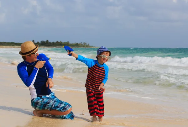 Father and son playing with water guns on the beach — Stock Photo, Image