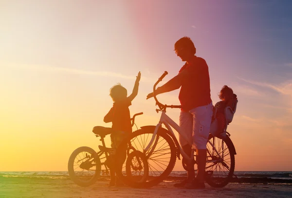 Батько з двома дітьми на велосипедах на заході сонця — стокове фото