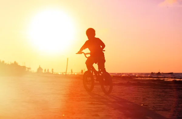 Menino pedalando bicicleta ao pôr do sol — Fotografia de Stock