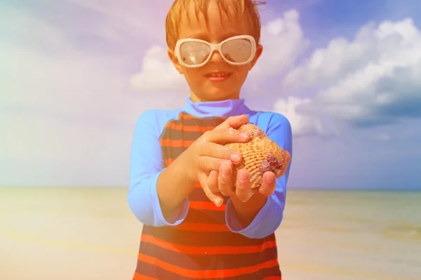 Mały chłopiec trzyma muszle na tropikalnej plaży latem — Zdjęcie stockowe
