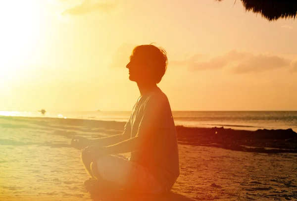 Jeune homme méditant à la plage du coucher du soleil — Photo