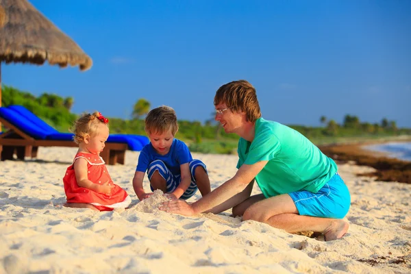 Vater und zwei Kinder spielen mit Sand am Strand — Stockfoto